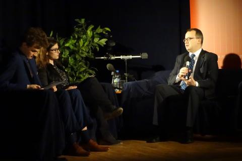 zdjęcie: na scenie stoją dwie ciemne kanapay, na których siedzi mężczyzna i trójka młodych ludzi