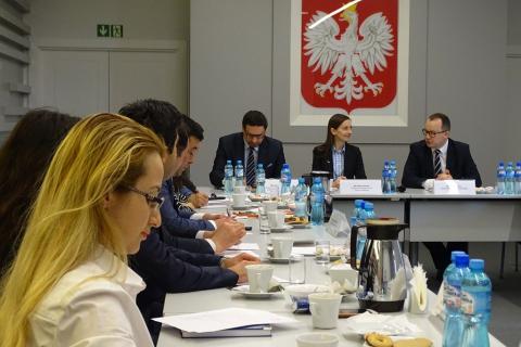 zdjęcie: po lewej strinie widać siedzące bokiem przy stole kilka osób, na wprost siedzą dwaj mężczyźni i kobieta