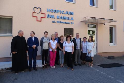 Zdjęcie: grupa ludzi przed budynkiem z napisem Hospicjum. Jest wśród nich ksiądz