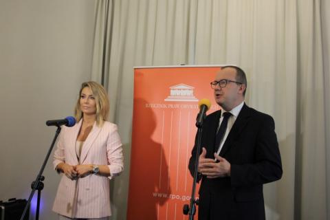 Koniebieta z długimi włosami i eleganckim różowym kostiumie i mężczyzna w garniturze na tle loga RPO