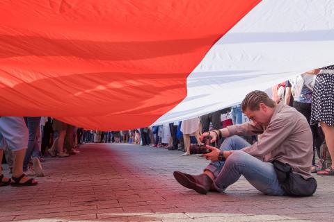 Człowiek w czasie demonstracji - siedzi pod bialo-czerwoną flaga