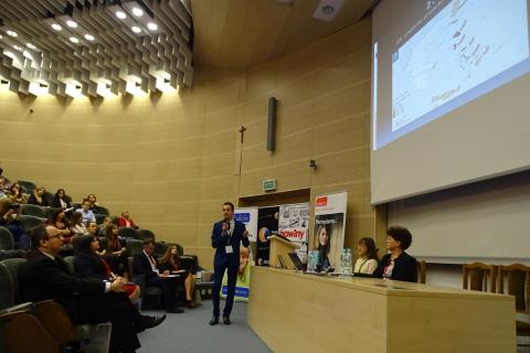 Zdjęcie: młody mężczyzna przedstawia prezentacje. Na ekranie mapa Polski ze strzałkami ze wschodu