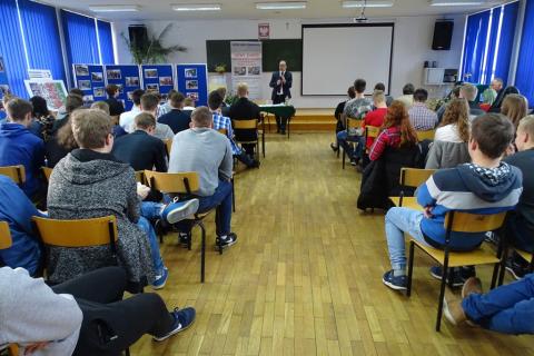 Sala w szkole. Mężczyzna mówi do młodych ludzi sfotografowanych z tyłu